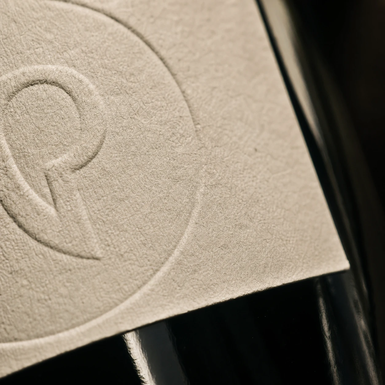 Blind-debossed BC monogram seal on uncoated paper wine label — extreme close-up